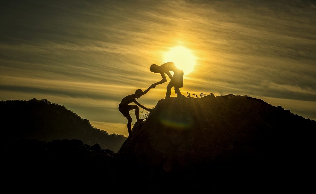 man helping his colleague get on top of a mountain